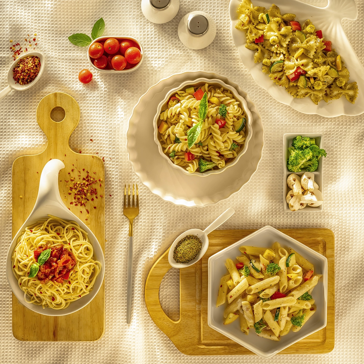 Overhead view of assorted pasta dishes with vegetables and seasonings arranged on a light textured table.